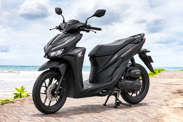 Matte-black Honda Vario125, front-left view, beside the ocean