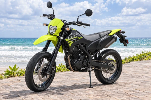 درّاجة Kawasaki KLX230 Supermoto باللونين الأخضر النيون والأسود، منظرة أمامية يسارية، بجانب المحيط