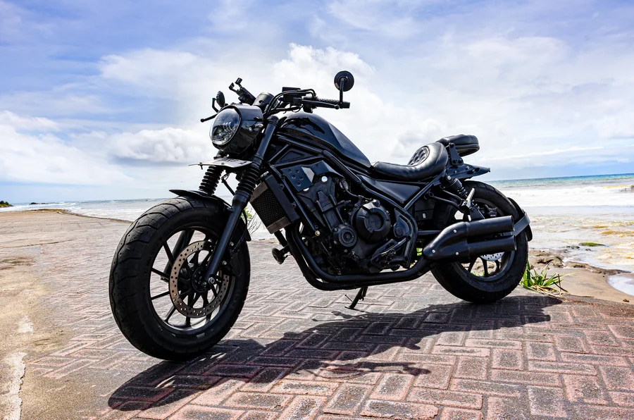 Black Honda Rebel 500 custom bobber with low ribbed rider seat, chopped rear and full true-dual open exhaust