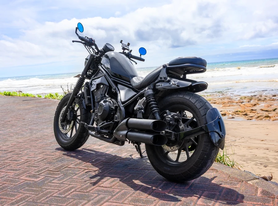 Black Honda Rebel 500 custom bobber with low ribbed rider seat, chopped rear and full true-dual open exhaust