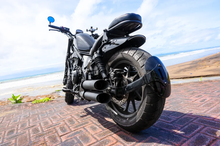 Black Honda Rebel 500 custom bobber with low ribbed rider seat, chopped rear and full true-dual open exhaust