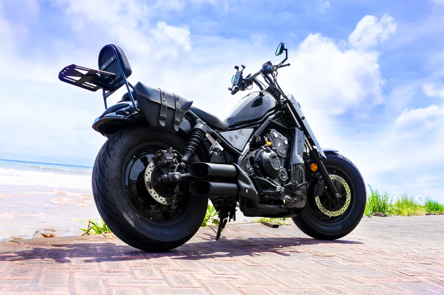 Černý motocykl Honda Rebel 500 ve stylu custom chopper s pohodlným sedadlem jezdce na motocyklu, zadním sedadlem spolujezdce a opěradlem, dvěma sedlovými brašnami a nosičem zavazadel