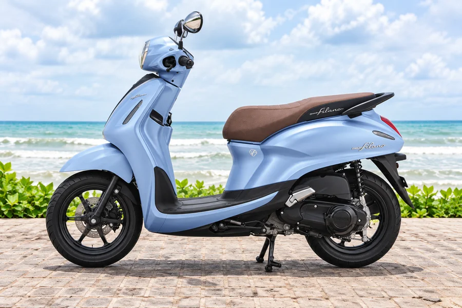 Blue Yamaha Grand Filano125 with brown seat, front-left view, beside the ocean